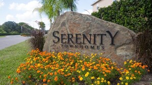 Un letrero de piedra con la inscripción 'Serenity Townhomes', rodeado de un jardín de flores anaranjadas y amarillas.
