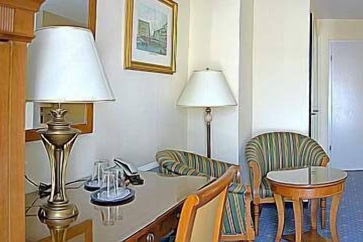 A hotel room with two beds, a small table, a chair, and a desk with a lamp.
