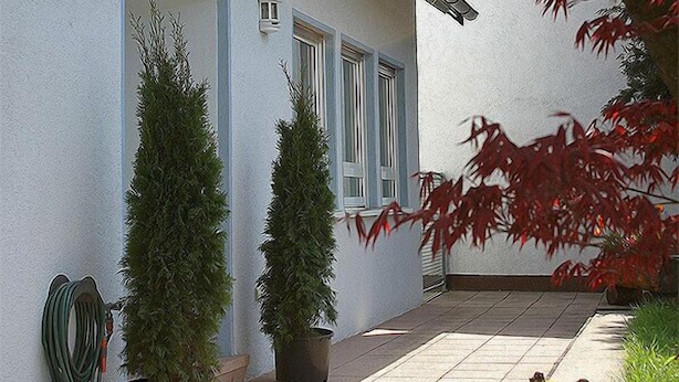 Une maison à l’extérieur blanc, dotée d’un porche et agrémentée de plantes en pot.