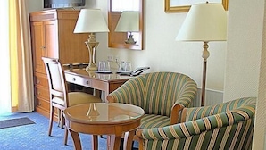 Une chambre d’hôtel avec un tapis bleu, un bureau en bois, deux fauteuils à rayures, une télévision, un miroir et un tableau encadré accroché au mur.
