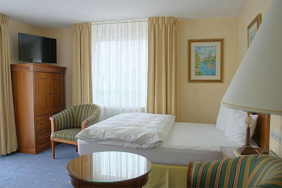 A hotel room with a bed, a chair, a television, a desk, and a lamp.