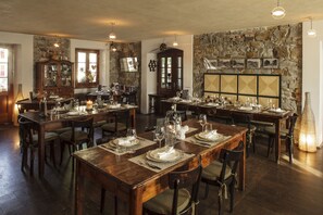 Un'area pranzo con tavoli di legno apparecchiati per diverse persone, pareti in pietra e una varietà di stoviglie.