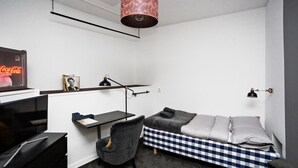 A compact room with a bed, desk, chair, and a hanging lamp. - Eight Rooms (Stockholm)