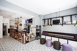 Un café moderno con suelo estampado, mostrador de madera y zona de estar con mesas y taburetes.