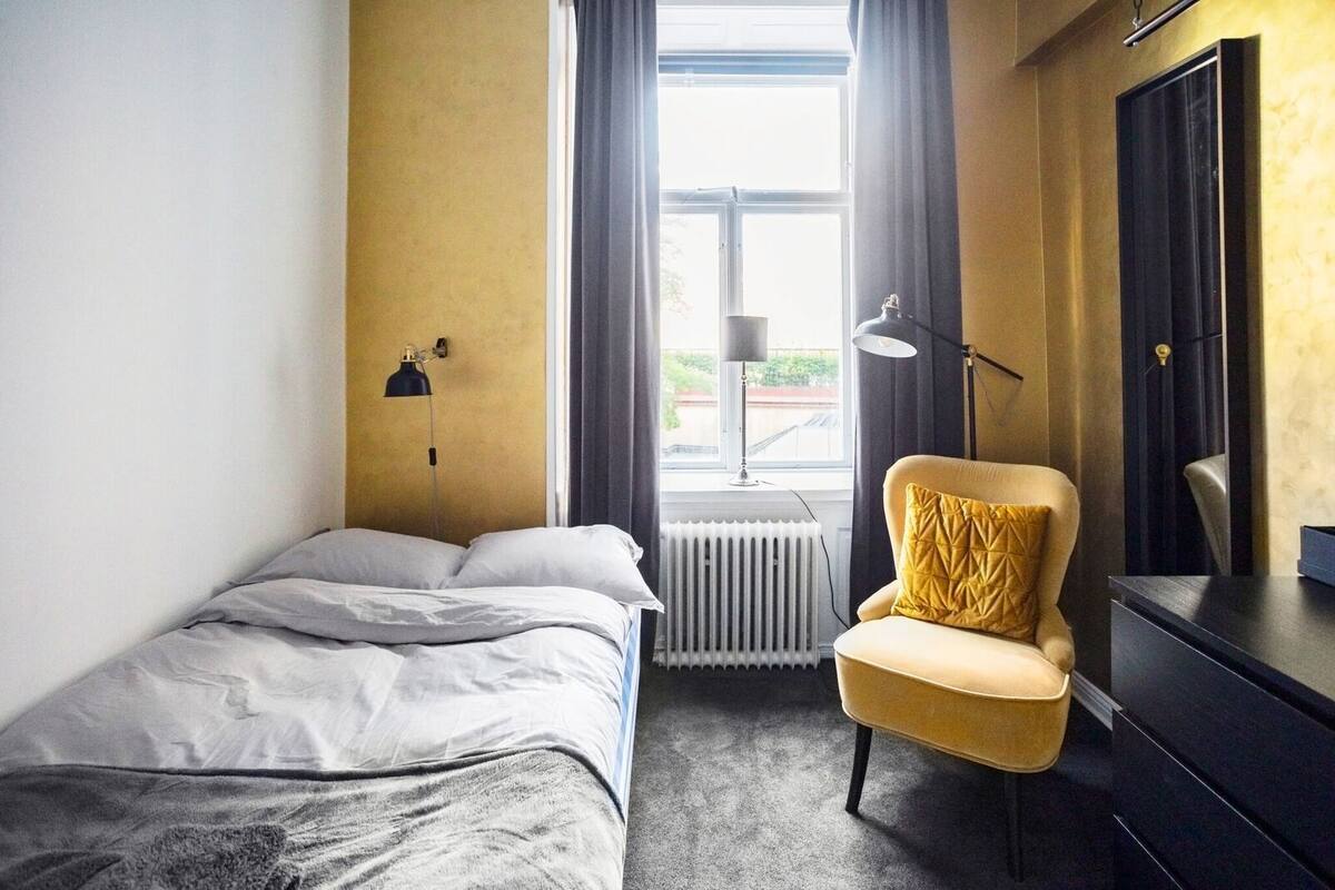 Una habitación de hotel con una cama, una silla, un escritorio, una lámpara y un radiador.