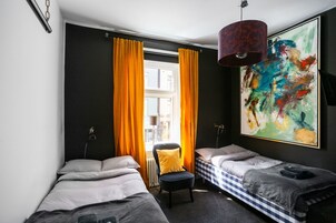 Una habitación de hotel con dos camas, una silla, un cuadro abstracto grande y una ventana con cortinas.