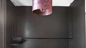 A compact, modern room with a dark color scheme, featuring a metallic refrigerator, a small wooden bench, a black storage unit, and a unique red and black pendant light. - Eight Rooms (Stockholm)