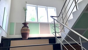 A staircase with metal railings, a potted plant, and a window with a view of greenery. - Tree House Apartment Songkhla (Songkhla)