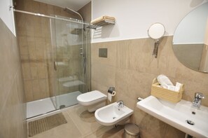 A modern bathroom with a glass-enclosed shower, a bidet, a sink, and a mirror. - Delco Naples (Naples)