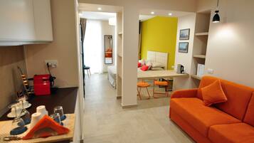 A modern hotel room with a sofa, a dining area, and a kitchen.