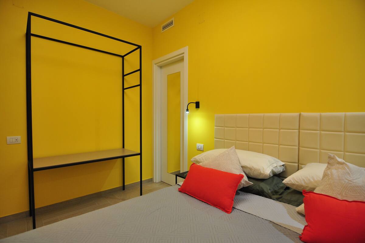 A room with a bunk bed, a bedside table, a wall-mounted light, and a door.