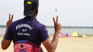 A person with a cap and a shirt labeled "Valamparti Sri Lanka" on a beach with kites in the background. - Valampuri Kite Resort (Kalpitiya)