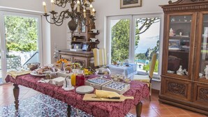 Comedor con una mesa dispuesta para el desayuno, una araña y vistas amplias por grandes ventanales.