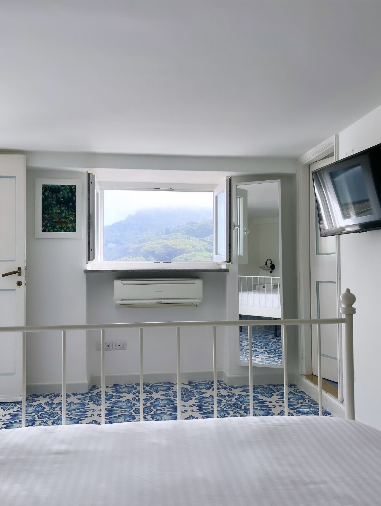 Un dormitorio con un ventanal grande, una cama, televisor montado y vistas a un paisaje montañoso.