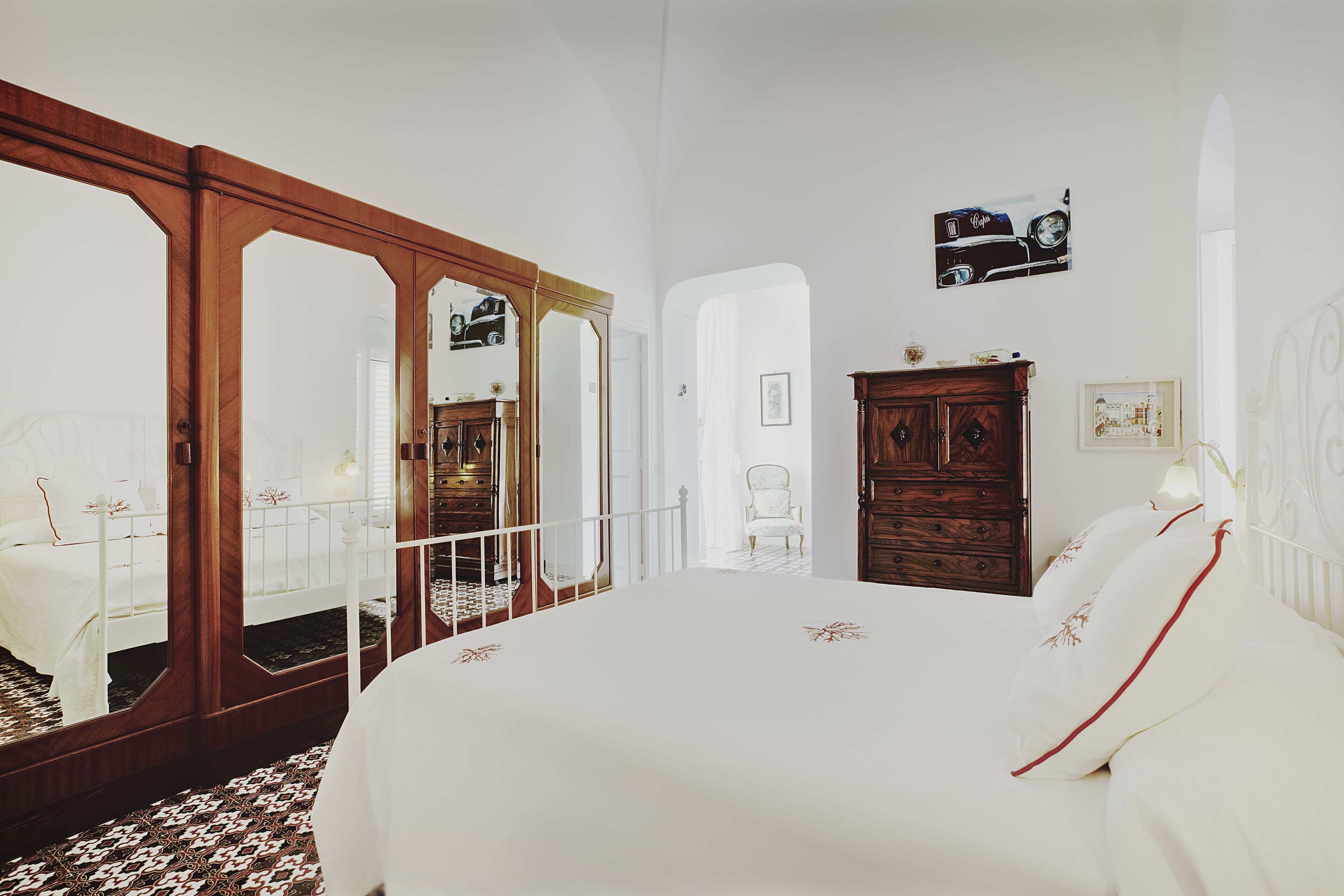 A bedroom with a large bed, a wooden wardrobe, a mirror, and a white chair.