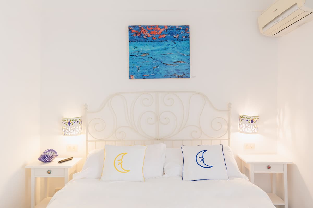 A neatly arranged bedroom with a bed, two bedside tables, a wall-mounted artwork, and a decorative lamp.
