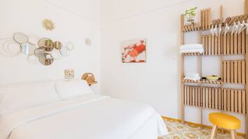 Een hotelkamer met een bed, een houten plank met handdoeken, een klein krukje en decoratie aan de muur.