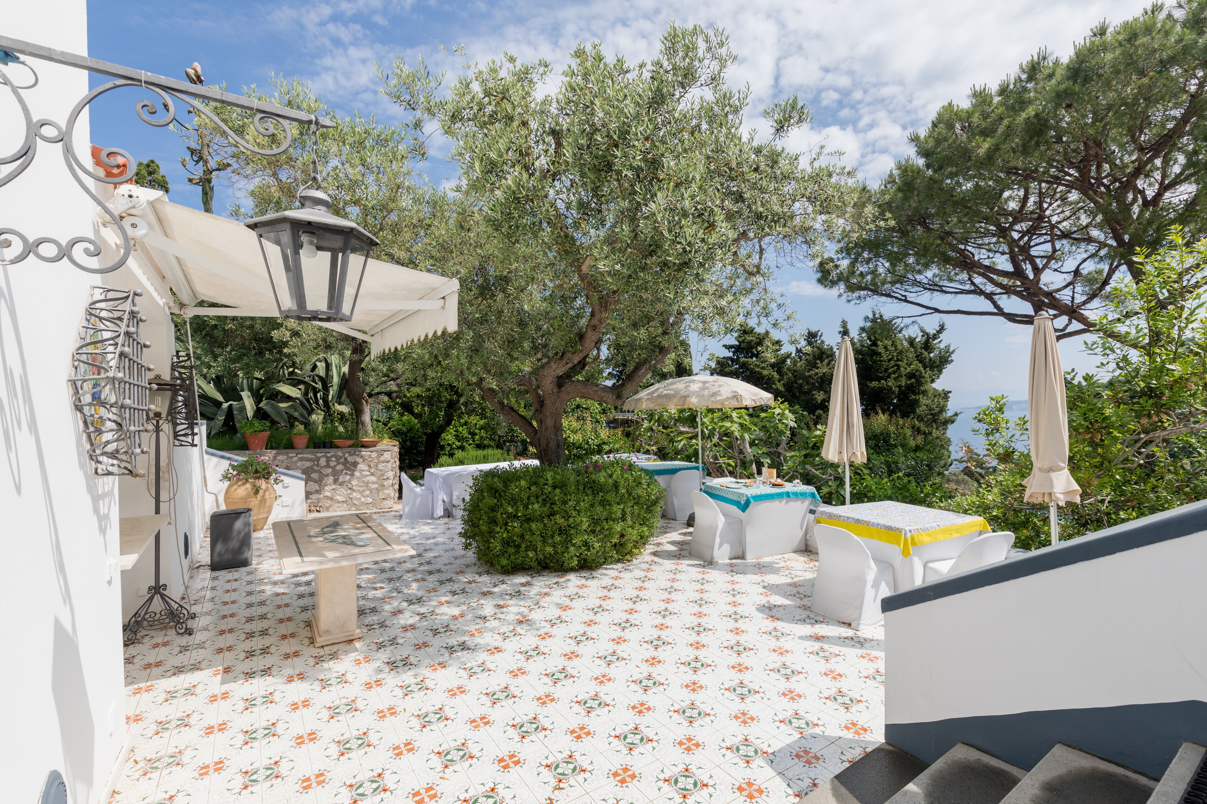 An outdoor patio with white tiled flooring, white furniture, and a pergola providing shade.