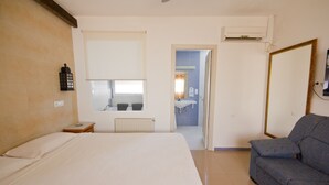 A hotel room with a bed, a small table, a sofa, a window, and a bathroom visible through an open door.