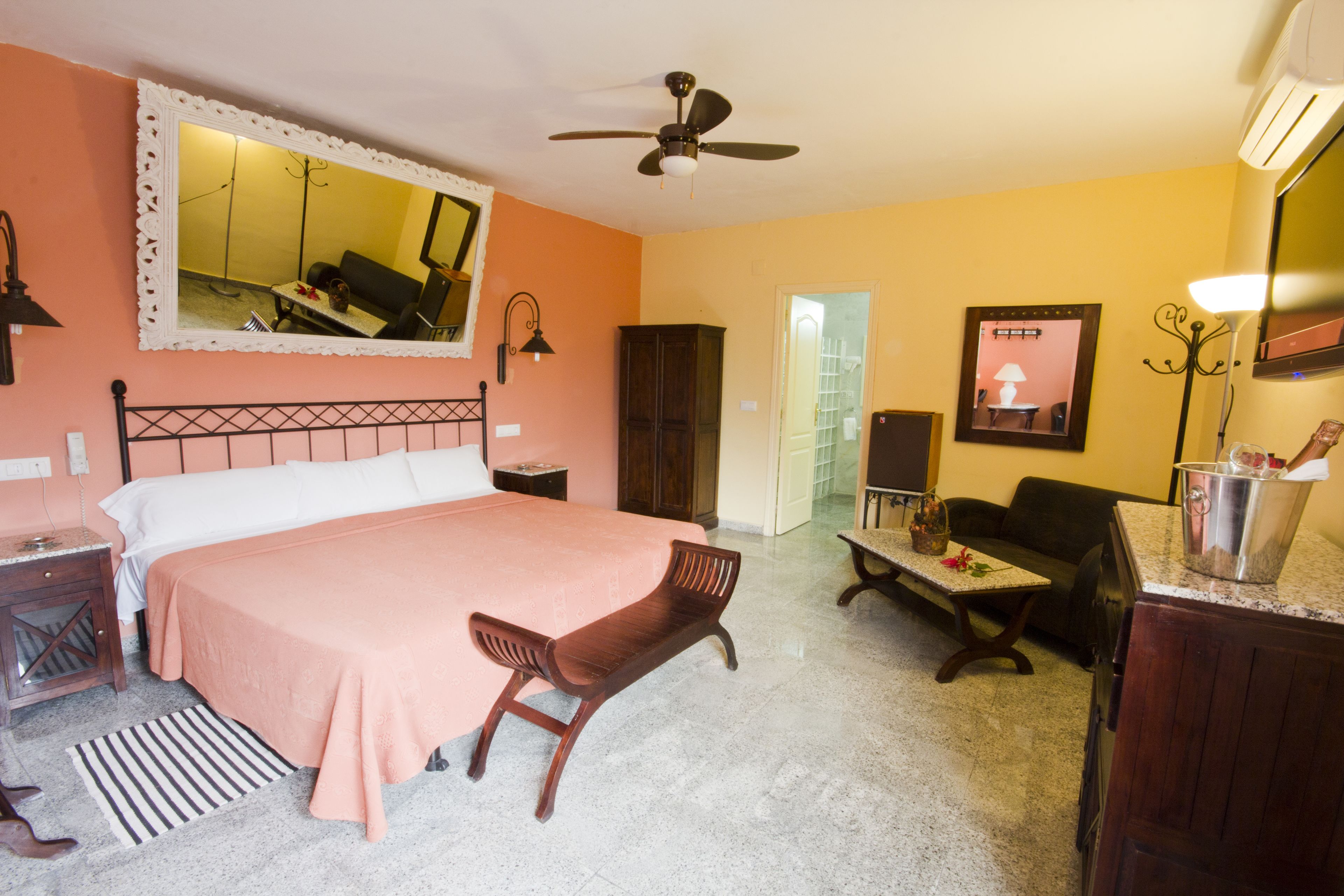 Une chambre d’hôtel équipée d’un lit, d’une chaise, d’un bureau, d’un miroir, d’un ventilateur de plafond et d’une kitchenette.