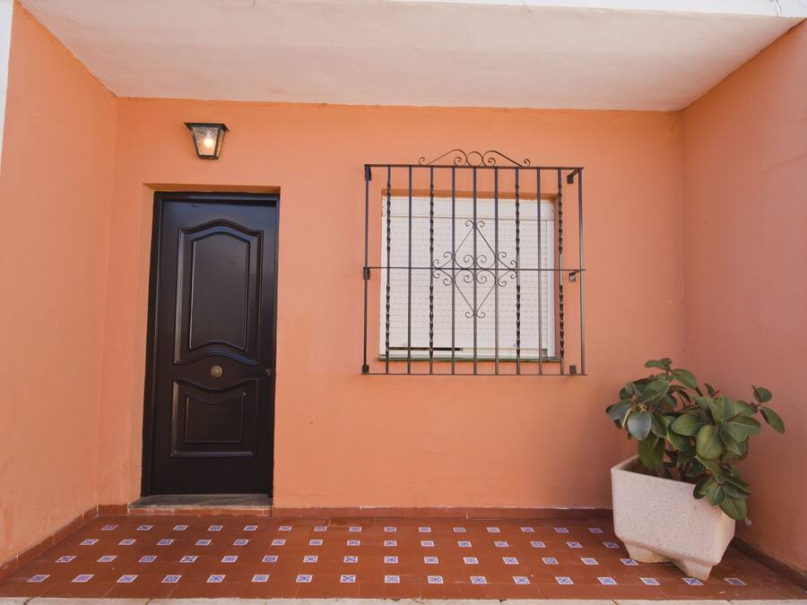 A black door, a window with decorative bars, and a potted plant on a tiled porch.