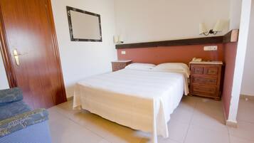 Un dormitorio con cama, mesita de noche, cómoda, espejo y puerta.