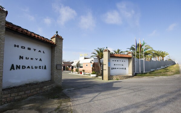 Ein Hotel Eingang mit der Beschilderung "Hostal Nueva Andalucía", einer gepflasterten Auffahrt und einem palmengesäumten Weg.