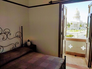 A room with a bed, a nightstand, and a view of a large white building with a dome through an open door. - Jerome's Old Havana Apartment (Havana)