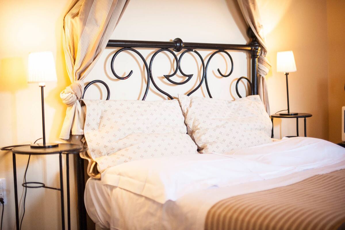 A neatly made bed with a patterned bedspread, two pillows, and a canopy. There are two bedside tables with lamps on either side of the bed.