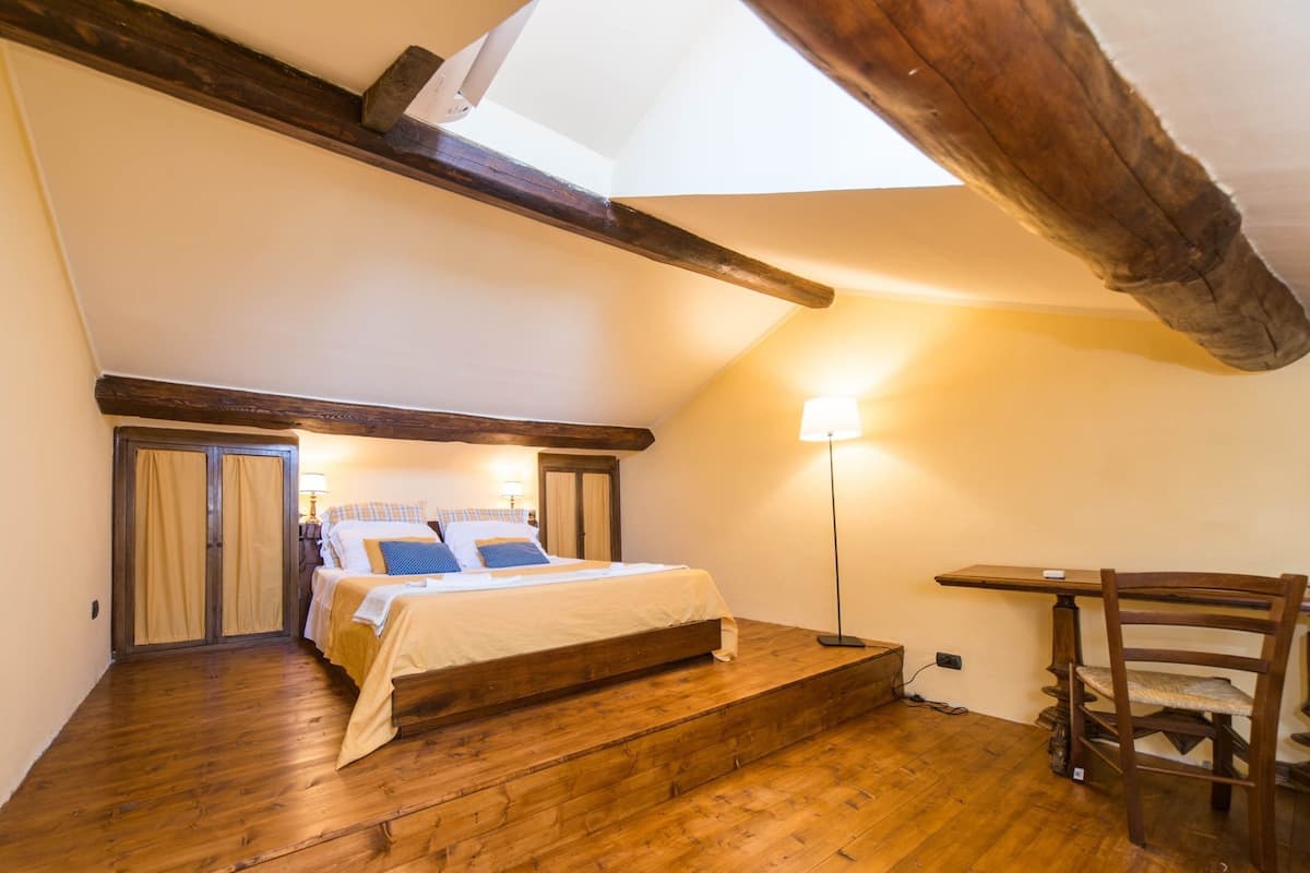 A cozy attic bedroom with a wooden bed, a nightstand, a lamp, and a chair.
