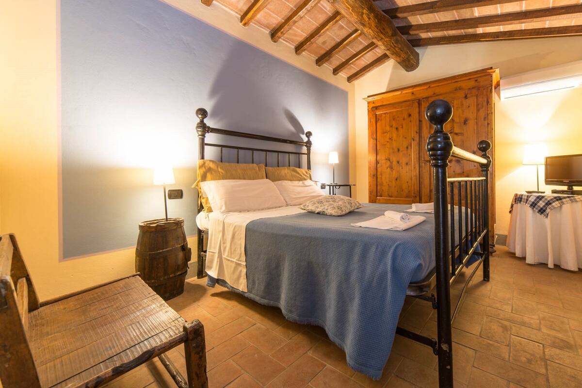 A bedroom with a wooden bed frame, a nightstand, a chair, and a wooden door.