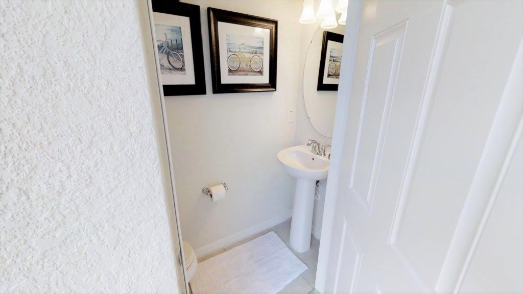 Un baño pequeño con un lavamanos blanco, un inodoro y dos cuadros en la pared.