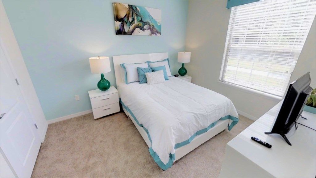 A bedroom with a bed, bedside tables, a TV, and a window.
