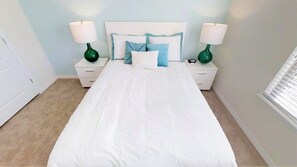 A neatly made bed with white bedding and blue pillows, flanked by two green bedside tables with lamps, in a room with light blue walls and a window on the right. - Aco234120 - Windsor At Westside Resort - 4 Bed 3 Baths Townhome (Kissimmee)