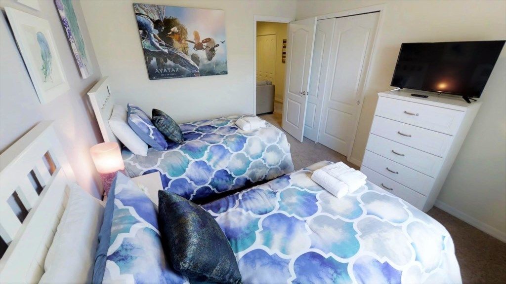 Une chambre avec deux lits, un téléviseur posé sur une commode et une porte donnant sur une autre pièce.