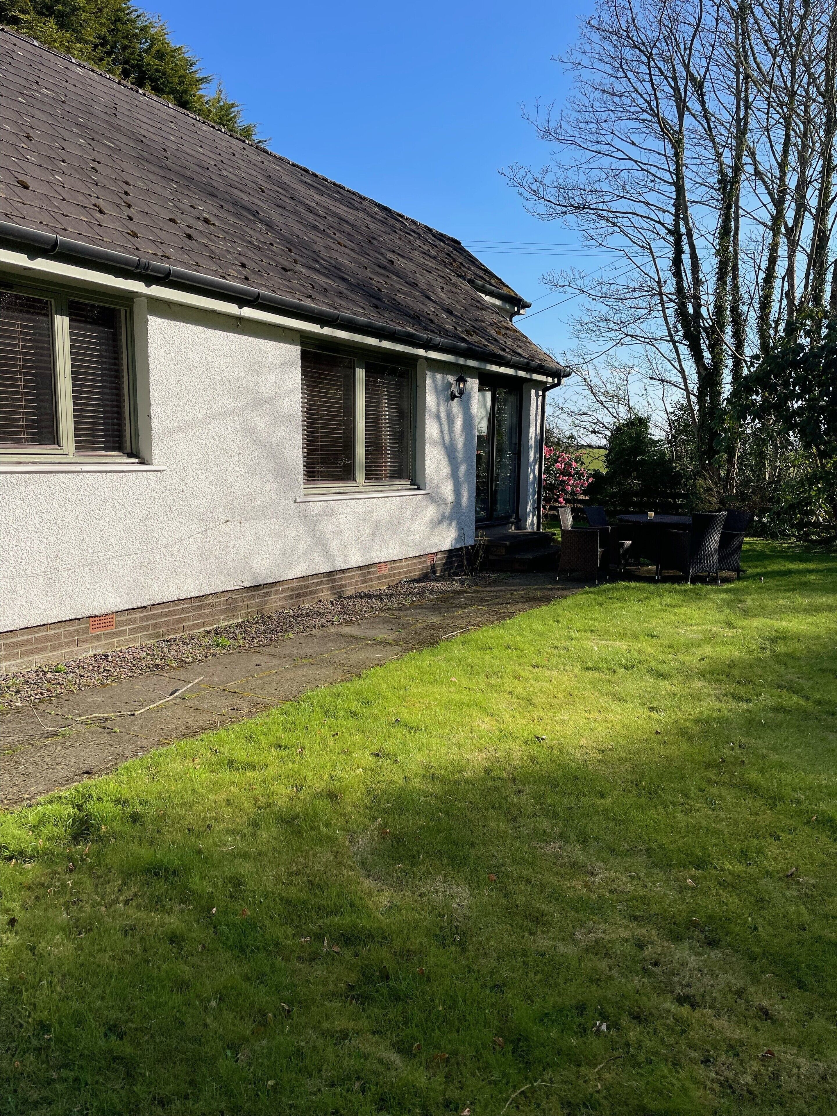A house with a sloped roof, a brick foundation, and a grassy yard.