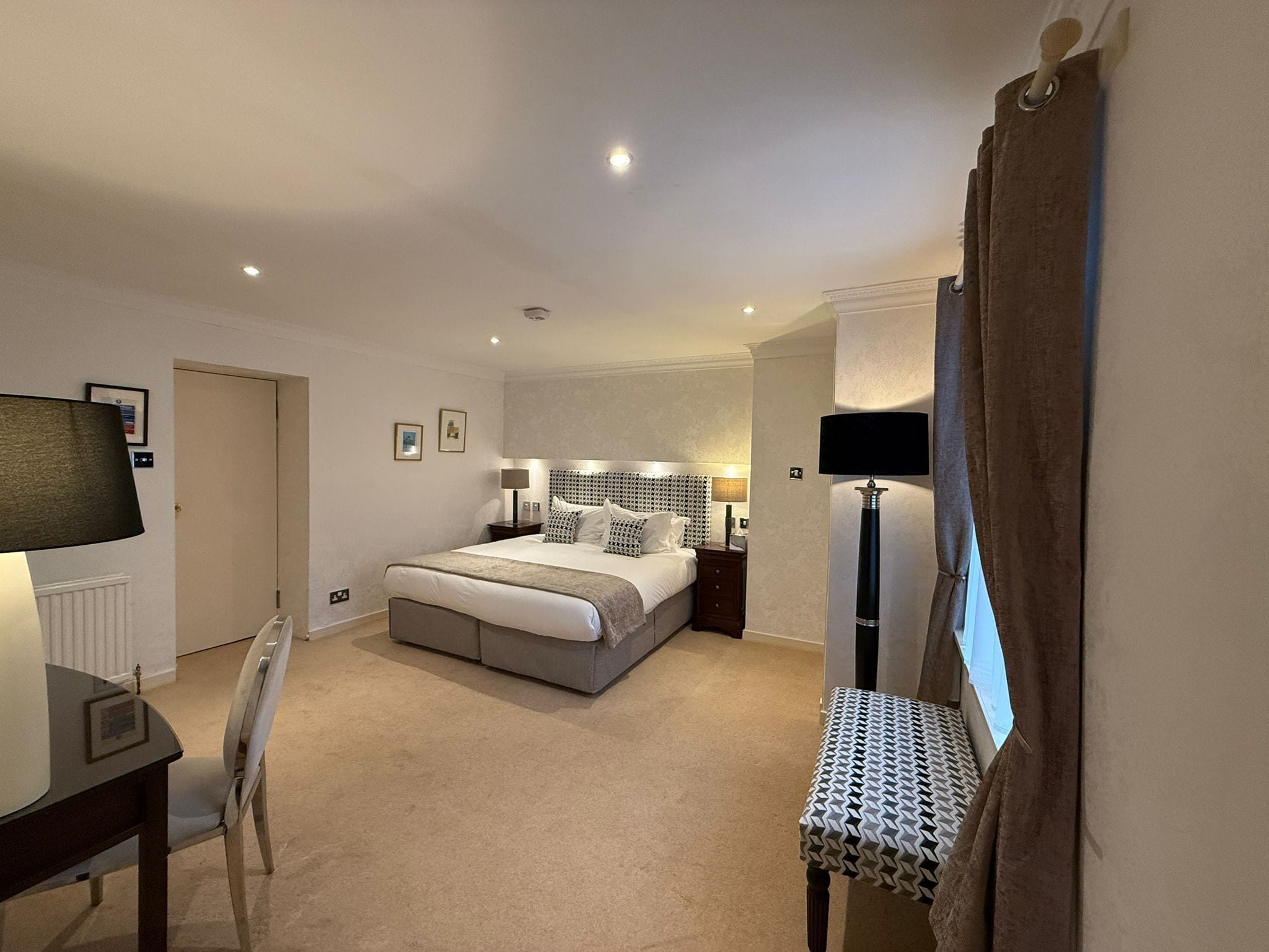A hotel room with a bed, bedside tables, a desk, a chair, and a floor lamp.