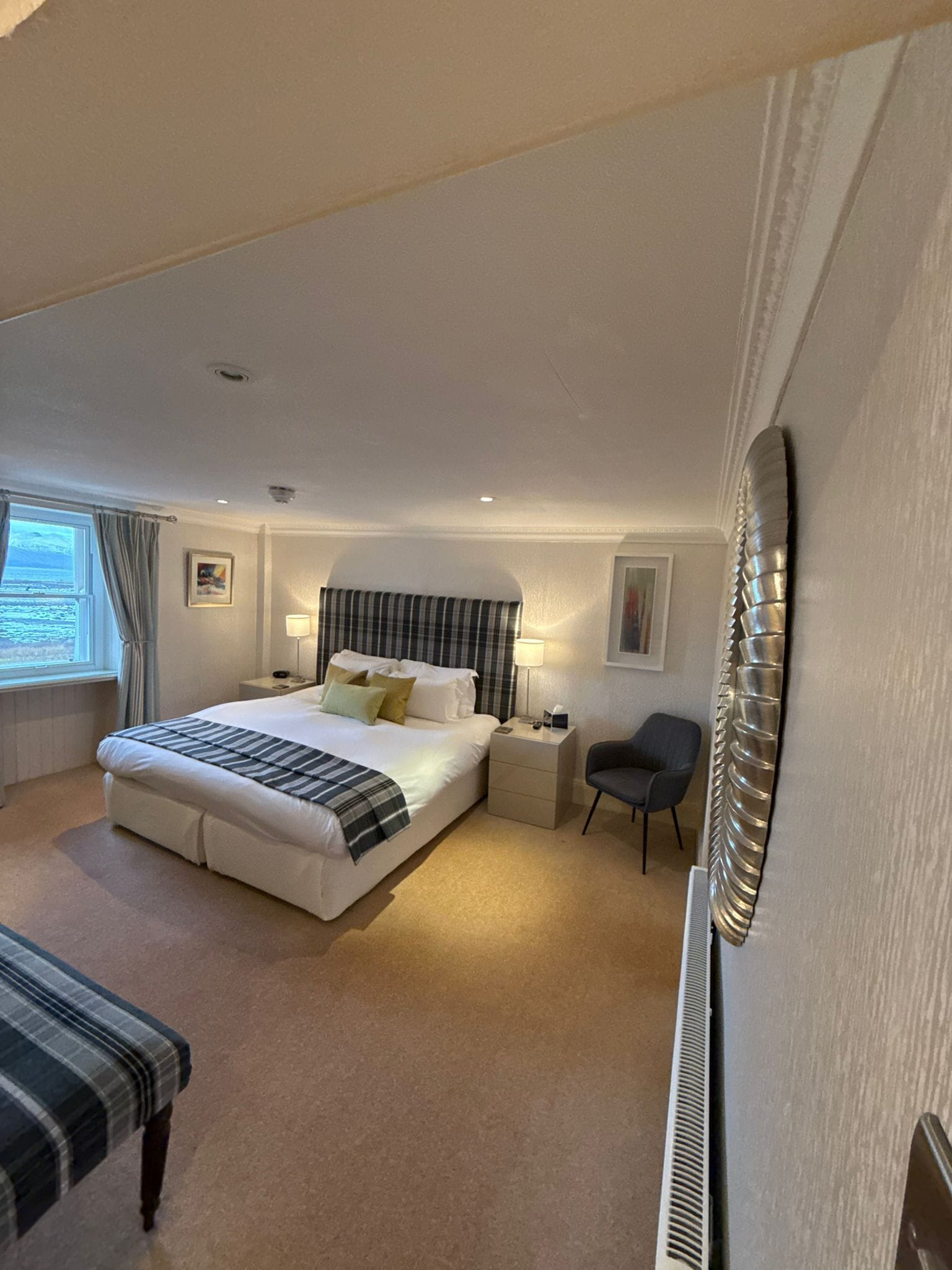 Ein Schlafzimmer mit einem großen Bett, Nachttischen, einem Sessel und Meerblick durch ein Fenster.