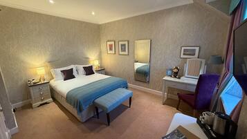 A hotel room with a bed, bedside tables, a desk, a chair, a mirror, and a window.