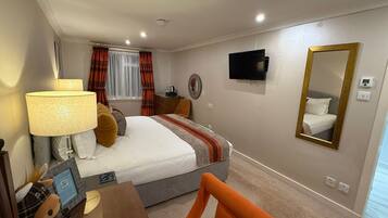 Habitación de hotel con cama, televisión, espejo, lámpara, silla y una pequeña mesa con un peluche.