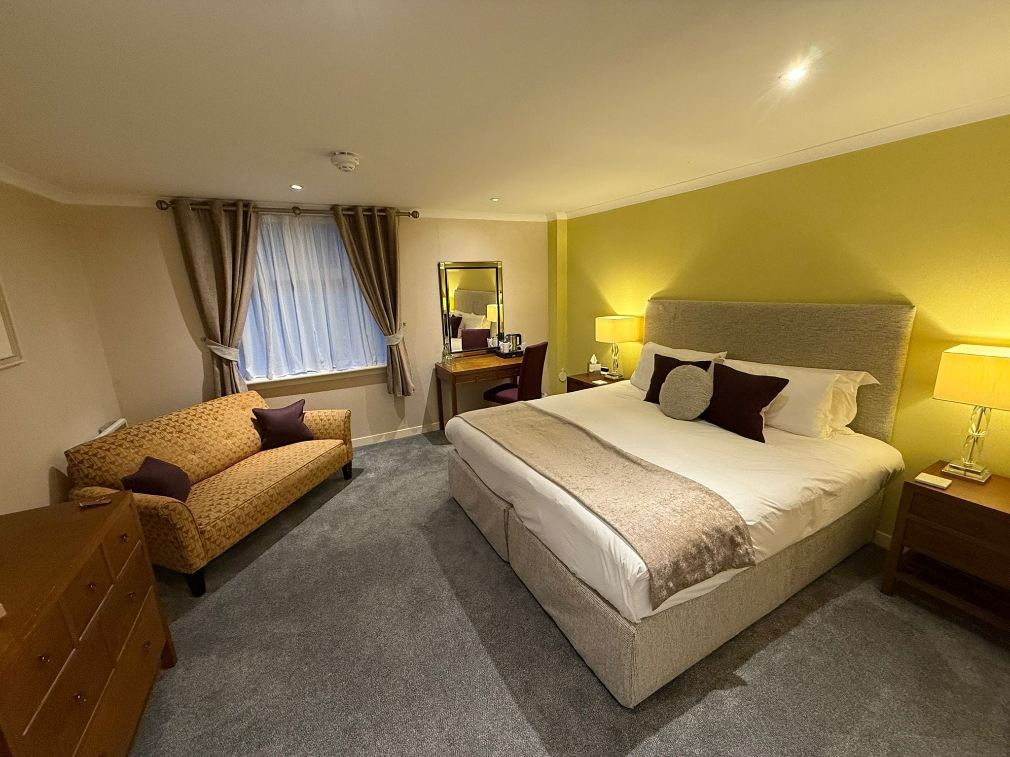 A hotel room with a large bed, a sofa, a desk, and a chair.