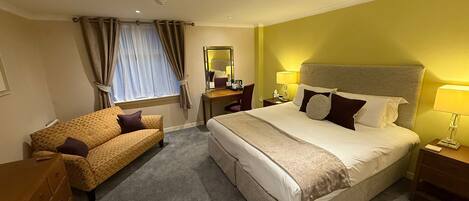 A hotel room with a large bed, a sofa, a desk, and a chair.