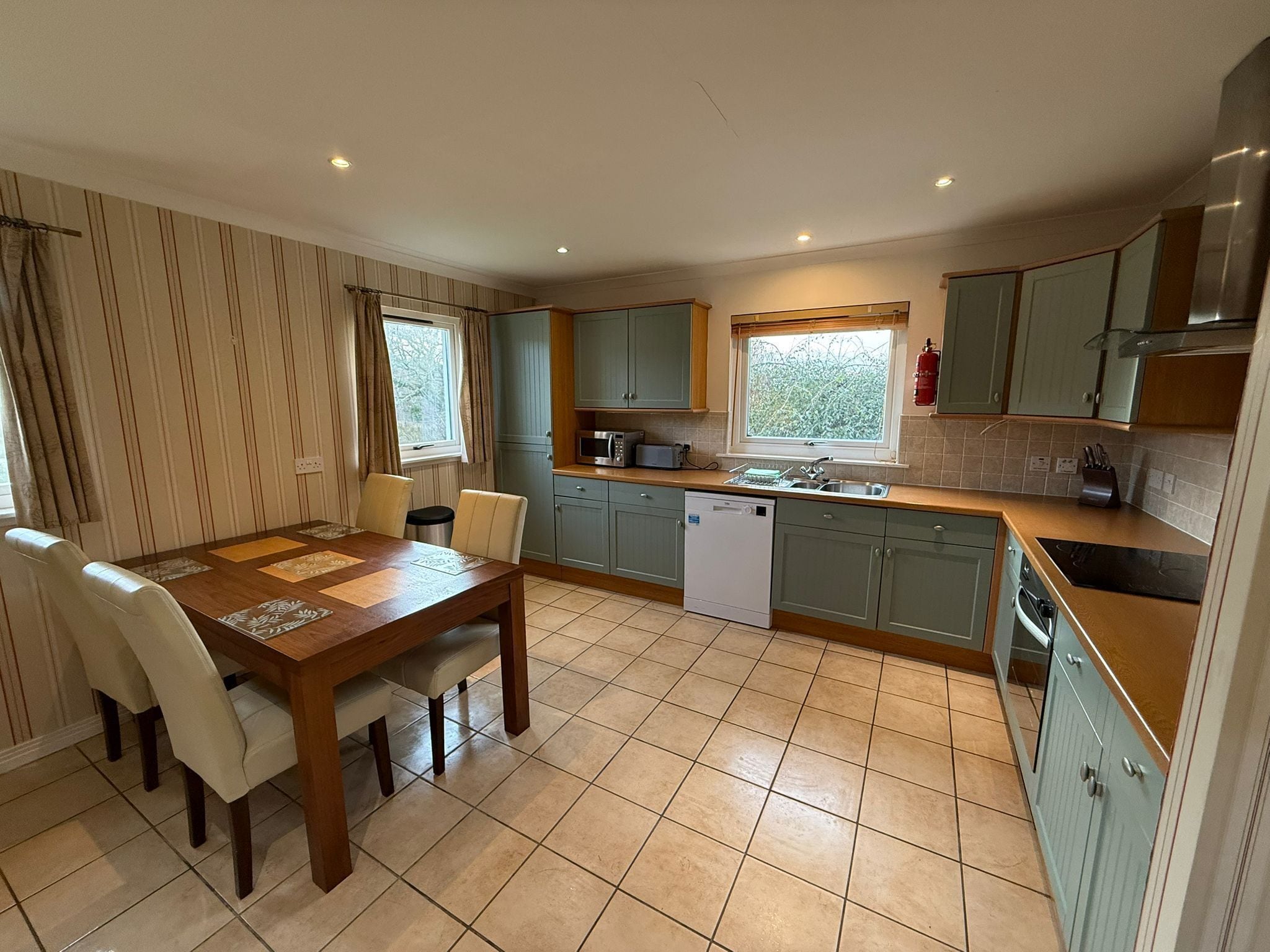 A compact kitchen with a dining table, chairs, a dishwasher, a microwave, and a window with curtains.