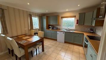 A compact kitchen with a dining table, chairs, a dishwasher, a microwave, and a window with curtains.