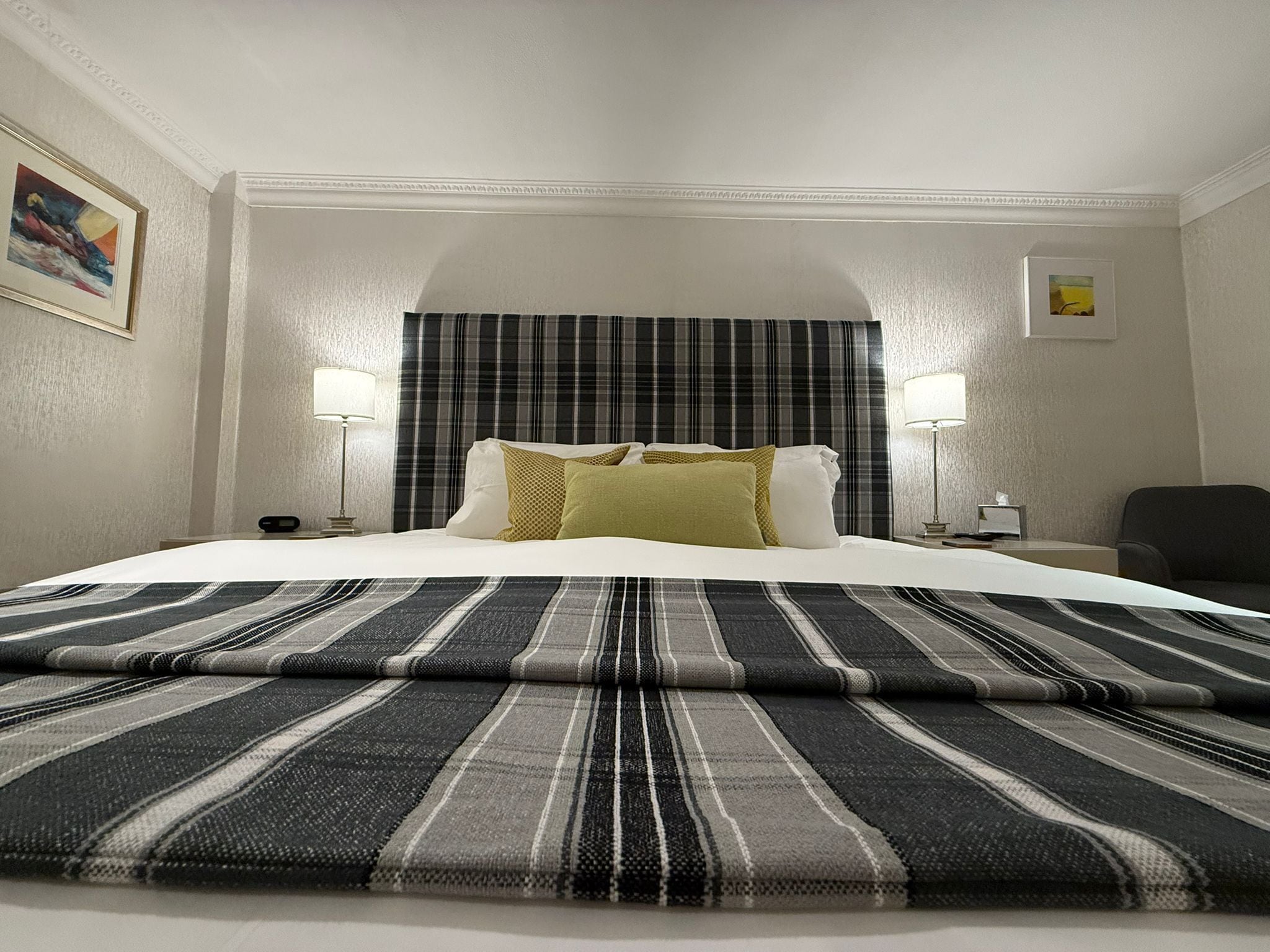 A hotel room with a large bed, two bedside lamps, a plaid curtain, and a framed picture on the wall.