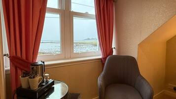 A room with a view of the sea, a chair, a table with a coffee maker, and a radiator.
