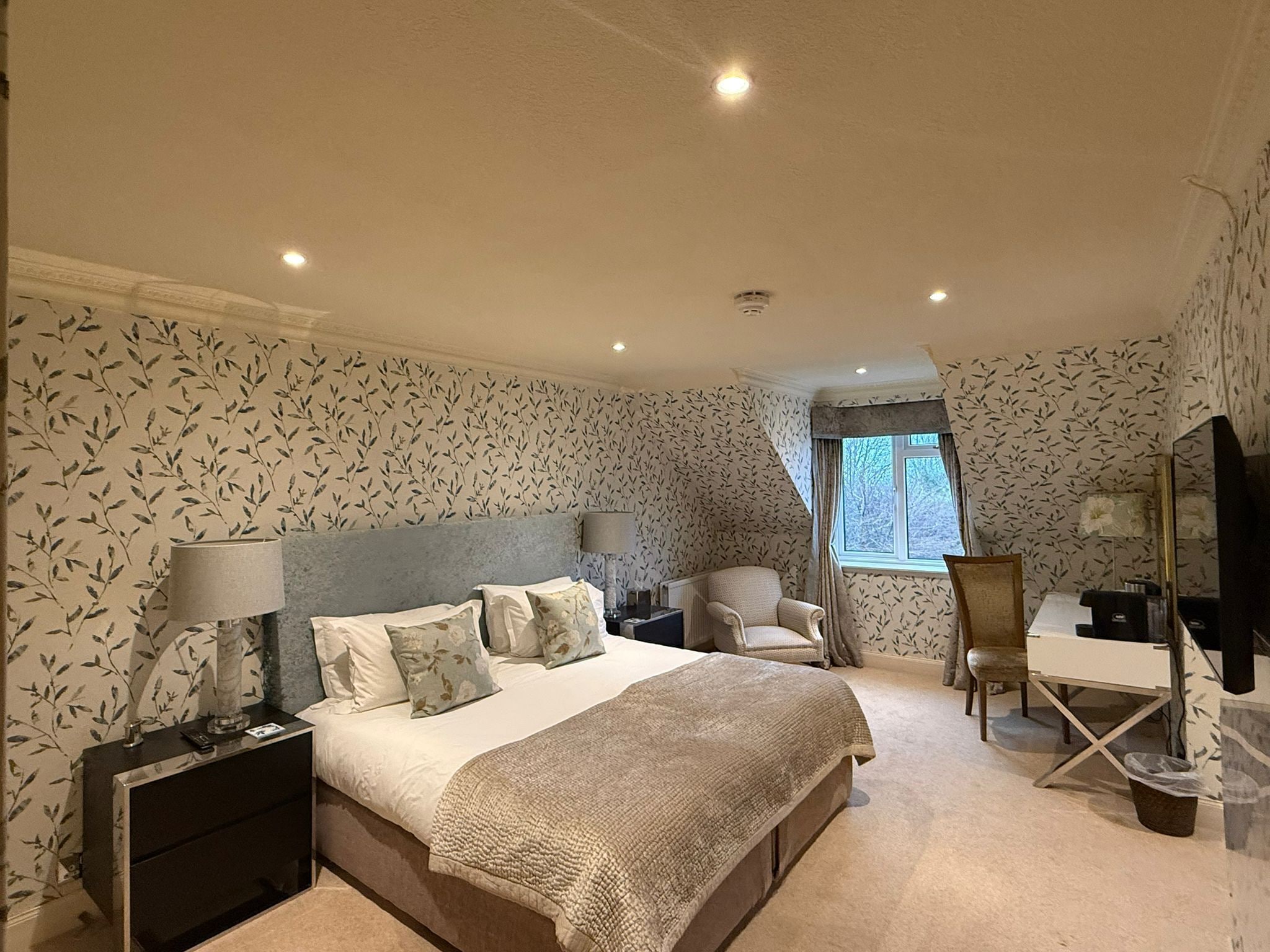 Een slaapkamer met een bed, nachtkastjes, een stoel, een bureau en een televisie.