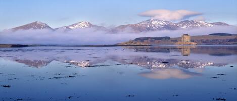 A tranquil lake with a castle on an island, surrounded by snow-capped mountains and a clear sky.