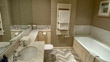 A modern bathroom with a large mirror, a marble sink, a toilet, and a bathtub.