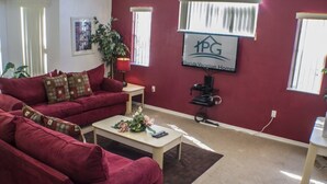 Una sala de estar con un sofá rojo, una mesa de centro y un televisor. Hay un cartel en la pared que dice "PG Florida Vacation Homes".